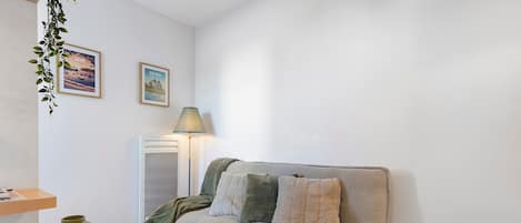 A cozy living room with a sofa, a lamp, a small table, and a decorative plant.