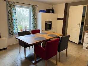 Un coin repas avec une table en bois, des chaises rouges, un buffet blanc et une fenêtre agrémentée de rideaux à motifs.