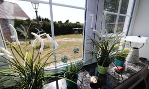 A conservatory with potted plants, a table lamp, and a view of a garden. - Gestrandet Vacation Home | Quiet Location | 20 Min. to the Baltic Sea | Sleeps up to 4 (Satow)