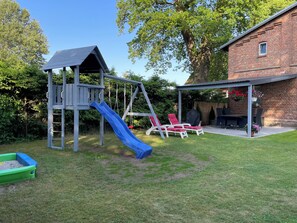 Un jardin avec une aire de jeux, un espace barbecue et une terrasse couverte.