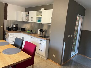 Une cuisine moderne avec des meubles blancs, un plan de travail en bois et un coin repas agrémenté d’une chaise rouge.