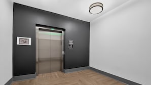 Un ascensor moderno con pantalla digital, señalización en la pared y suelo de madera con diseño tipo espiga.