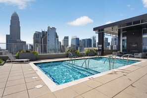 A rooftop pool with city skyline views, lounge chairs, and a covered seating area. - Stylish Stay Near Everything (Charlotte)