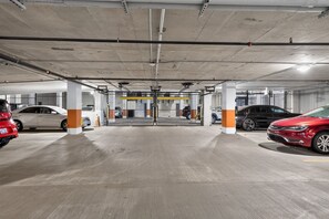 Un estacionamiento de varios niveles con pilares de hormigón, entrada con barreras y varios coches aparcados.