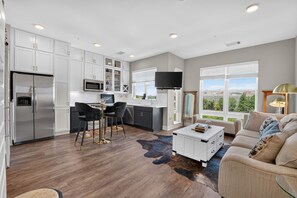 A modern kitchen with white cabinets, a stainless steel refrigerator, and a dining area with black chairs. - Stylish Stay Near Everything (Charlotte)