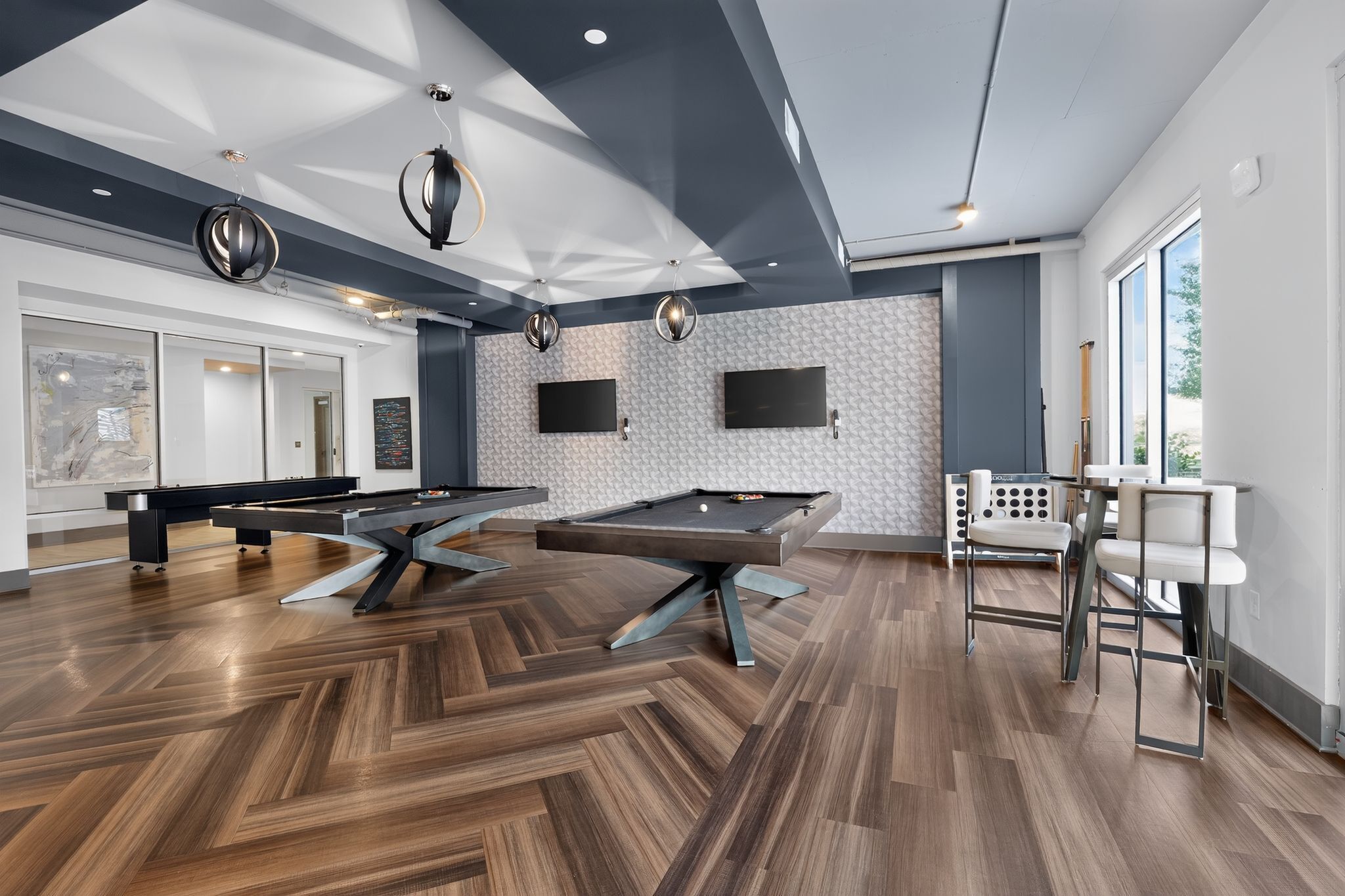 A modern recreational room with pool tables, a billiards setup, and large windows.