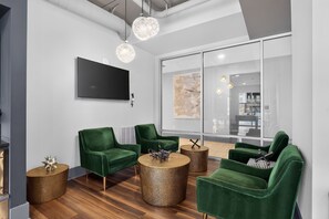 A modern office space with green upholstered chairs, a round coffee table, and a flat-screen TV mounted on the wall. - Stylish Stay Near Everything (Charlotte)