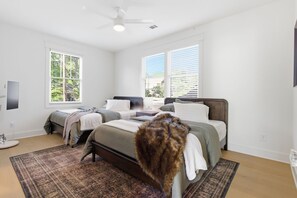 Ein Schlafzimmer mit zwei Betten, einem Deckenventilator und großen Fenstern mit Jalousien.
