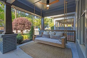 Ein überdachter Balkon mit einer Holzliege, einer Ziegelstütze und Blick auf die Straße.