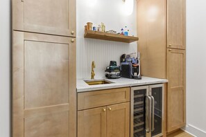 Eine Küche mit Holzschränken, einer Edelstahl-Spüle, einem integrierten Weinkühler und einer Kaffeemaschine.