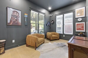 Ein Zimmer mit zwei Sesseln, einem Teppich, einem Schreibtisch und gerahmten Kunstwerken an den Wänden.