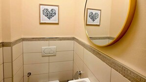 Une petite salle de bain avec des toilettes, un lavabo et un miroir. Deux tableaux encadrés sont accrochés au mur.