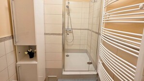 A shower with a glass door, a white towel rack, and a small cabinet with a flower.