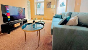 Un salon avec une télévision, un canapé, une table basse et une fenêtre.