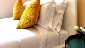 A bed with white bedding and two yellow pillows, a bedside table with a vase of flowers, and a framed picture on the wall.