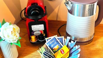 Una cafetera, un hervidor y cápsulas de café sobre una mesa de madera.