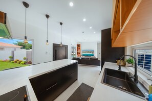 Eine moderne Küche mit einer zentralen Kochinsel, Pendelleuchten und Blick auf einen Pool.