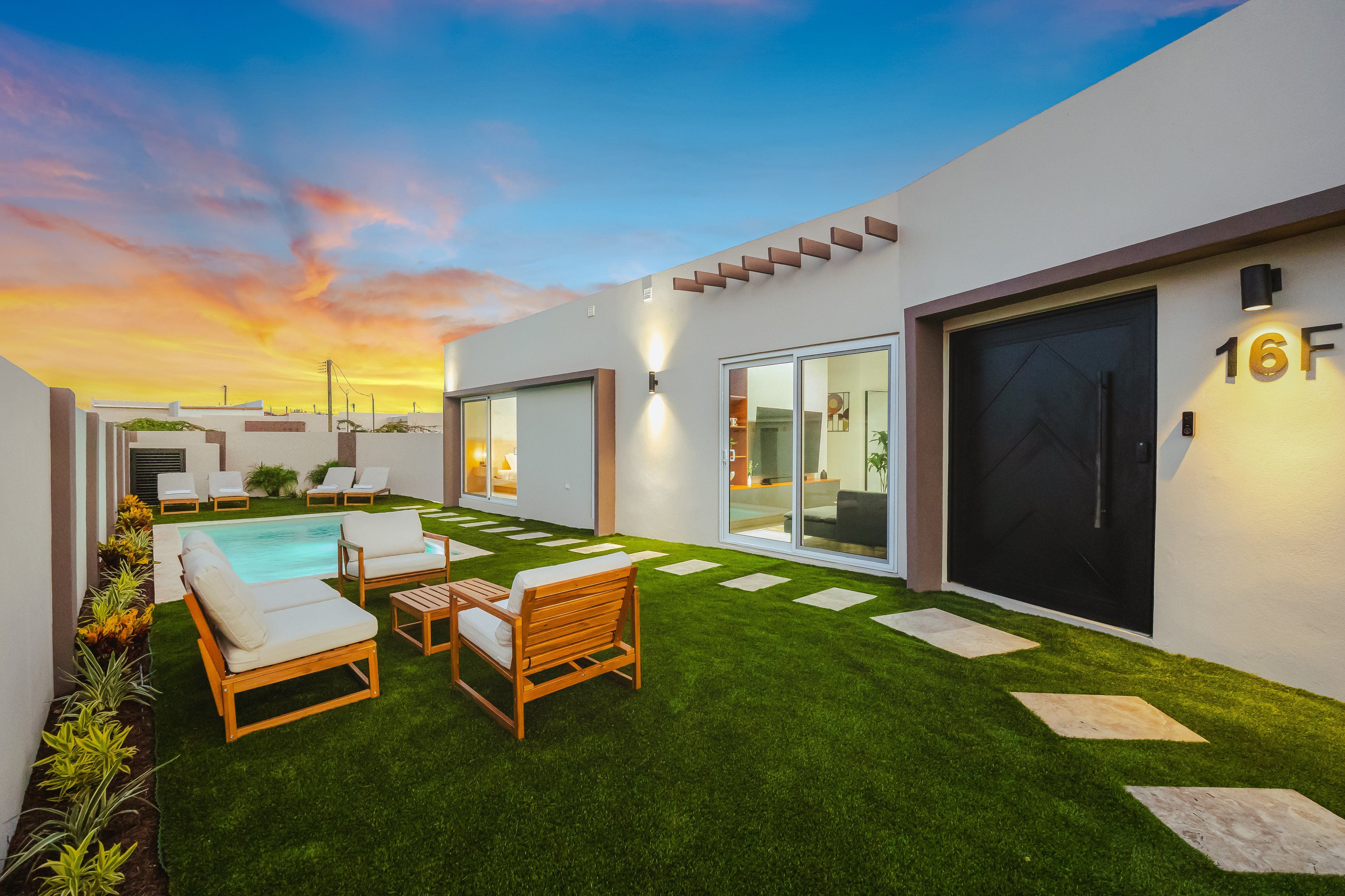A modern outdoor living area with a pool, lounge chairs, and a well-maintained lawn.
