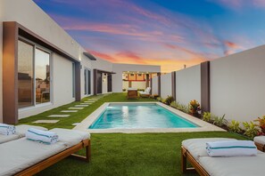 Ein moderner Poolbereich im Freien mit Kunstgrashalters, Liegestühlen und Blick auf den Sonnenuntergang.