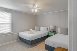 Une chambre avec deux lits, un ventilateur de plafond, une table de chevet avec une lampe et une fenêtre avec des stores.