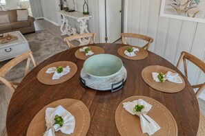 A round wooden dining table with a central bowl, surrounded by six chairs with woven placemats and white napkins tied with greenery. - Mystic C's Inlet Side Escape (Murrells Inlet)
