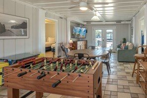 A room with a foosball table, a dining table, a sofa, and a television mounted on the wall. - Mystic C's Inlet Side Escape (Murrells Inlet)