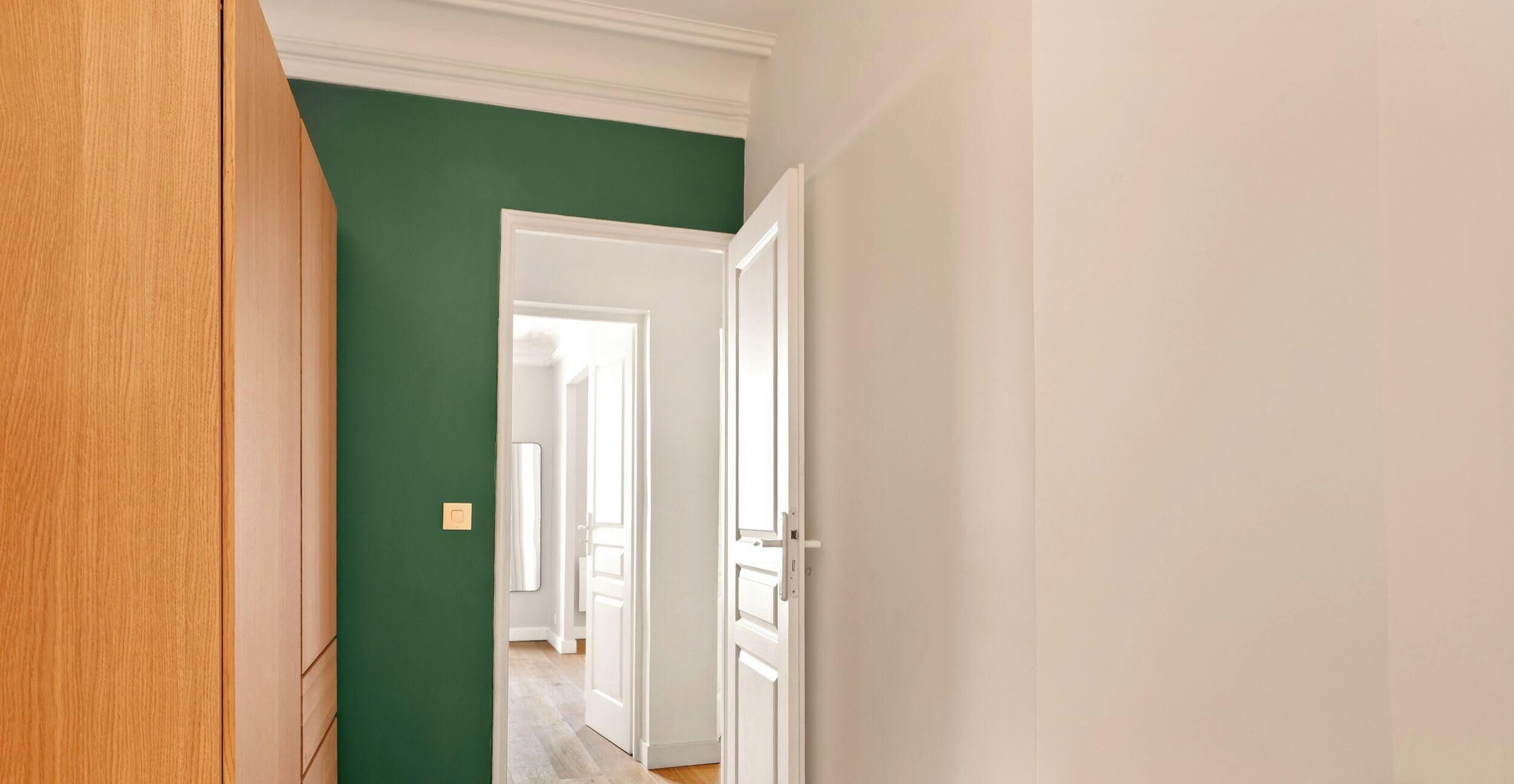 A hallway with a green wall, white door, and wooden paneling.