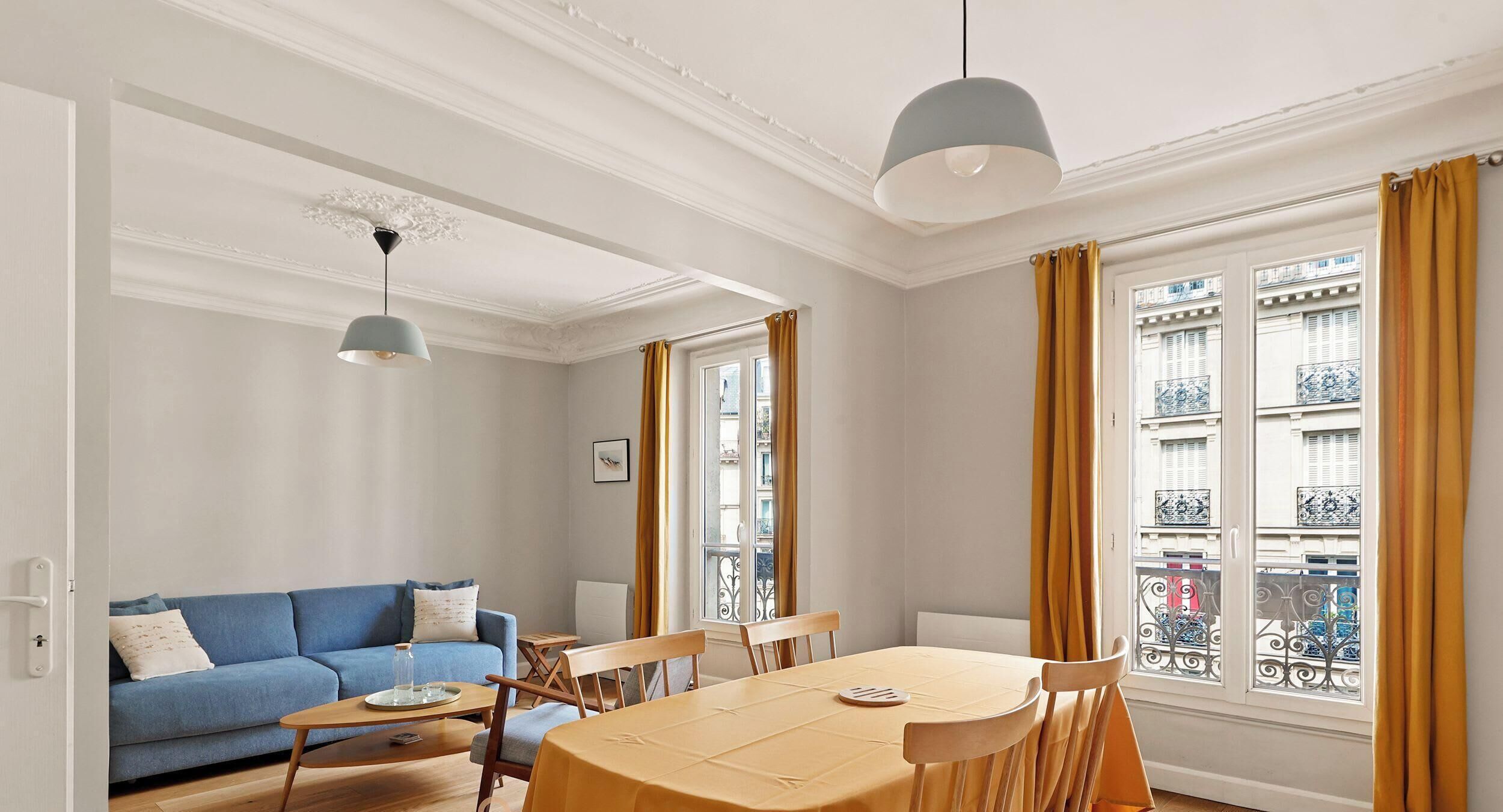 A room with a blue sofa, wooden dining table, and chairs, a small side table, and a pendant light.