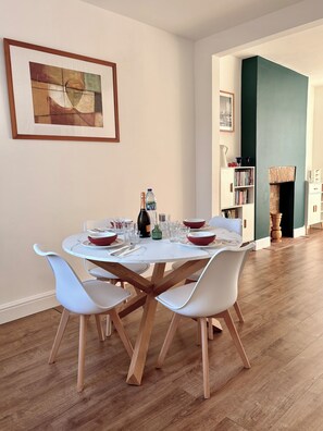 A dining area with a round table, white chairs, and a bottle of champagne. - Spacious Victorian House - E6 London (London)