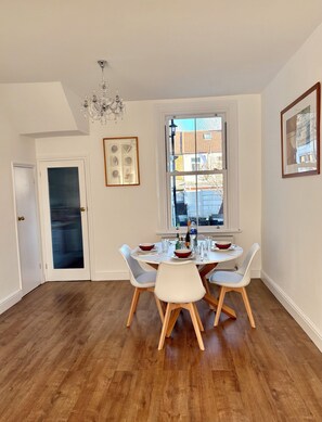 A dining area with a table set for four, a chandelier, and a window with a view of buildings. - Spacious Victorian House - E6 London (London)