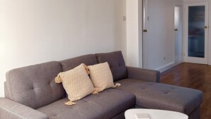 Een moderne woonkamer met een grijze bank, twee gekleurde kussens, een witte salontafel en een kristallen kroonluchter.