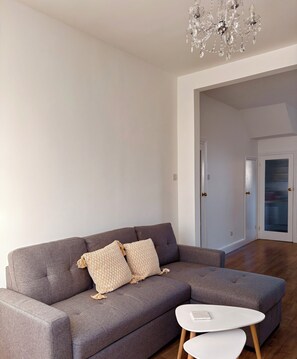 A modern living room with a grey sofa, two patterned cushions, a white coffee table, and a crystal chandelier. - Spacious Victorian House - E6 London (London)