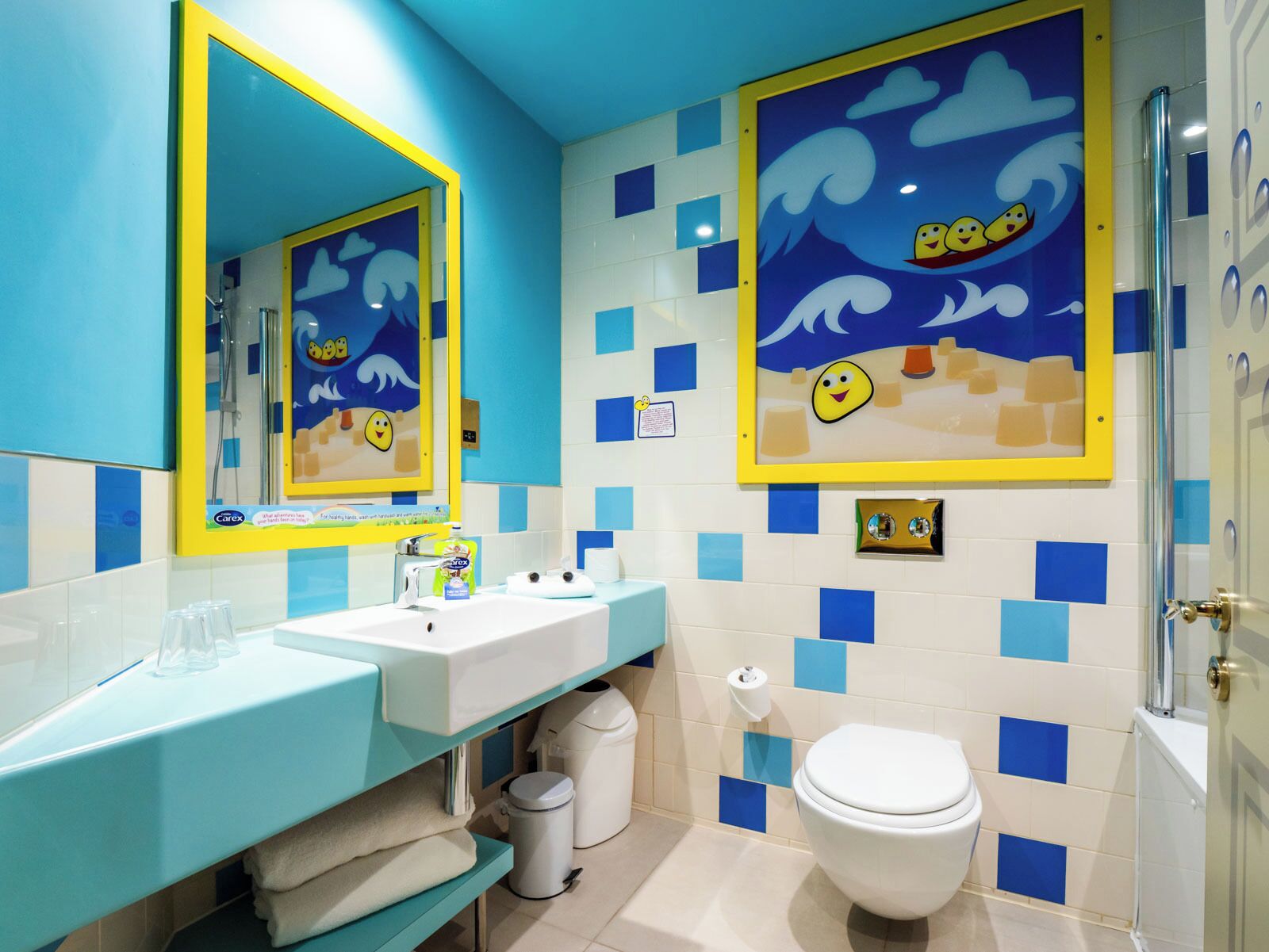 A bathroom with a blue and white tiled wall, a sink with a mirror, a toilet, and a shower area.