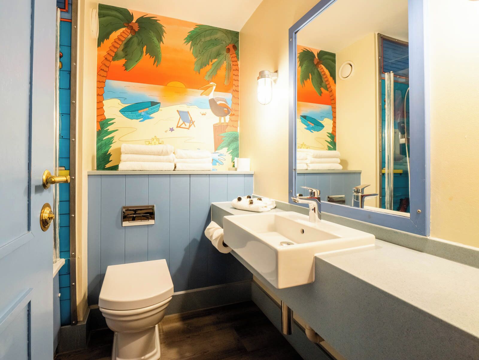 Une salle de bain équipée de toilettes, d’un lavabo et d’une fresque murale représentant une scène de plage.