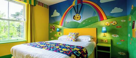 Habitación infantil con cama, ventana y un mural que muestra un arcoíris y caras sonrientes.