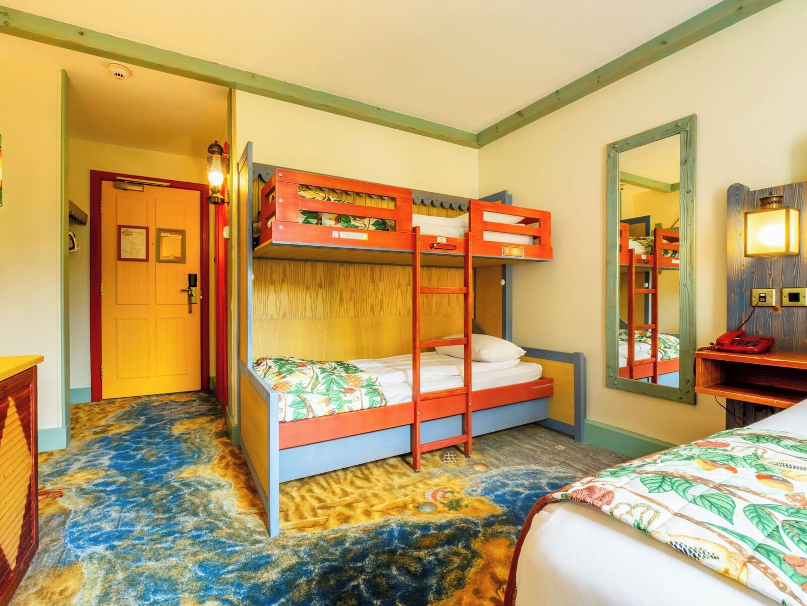 A room with bunk beds, a wooden door, a mirror, and a patterned carpet.