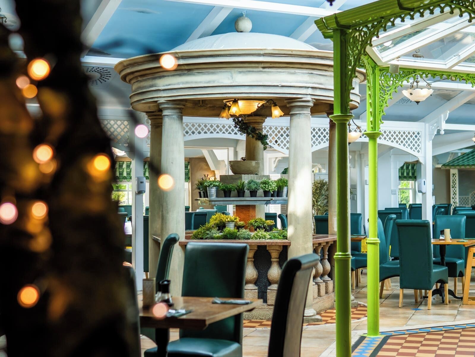 A covered outdoor seating area with tables and chairs, a central decorative structure, and potted plants.