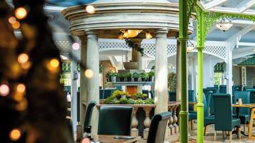 A covered outdoor seating area with tables and chairs, a central decorative structure, and potted plants.