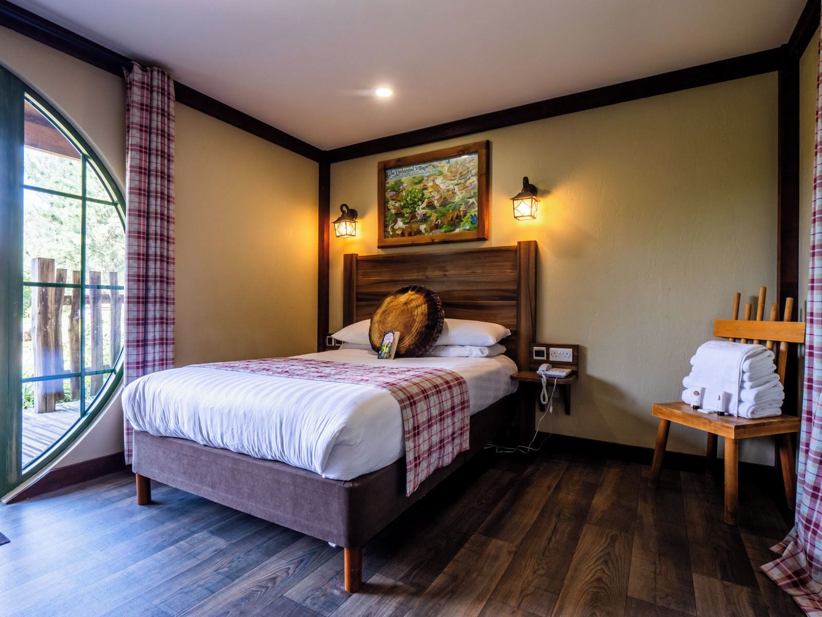 A hotel room with a bed, a nightstand, a lamp, a painting, and a view of the outdoors.