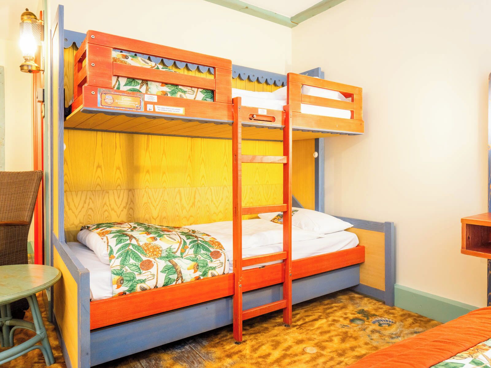A bunk bed with a ladder, a small table, and a chair in a room with wooden walls and a patterned floor.