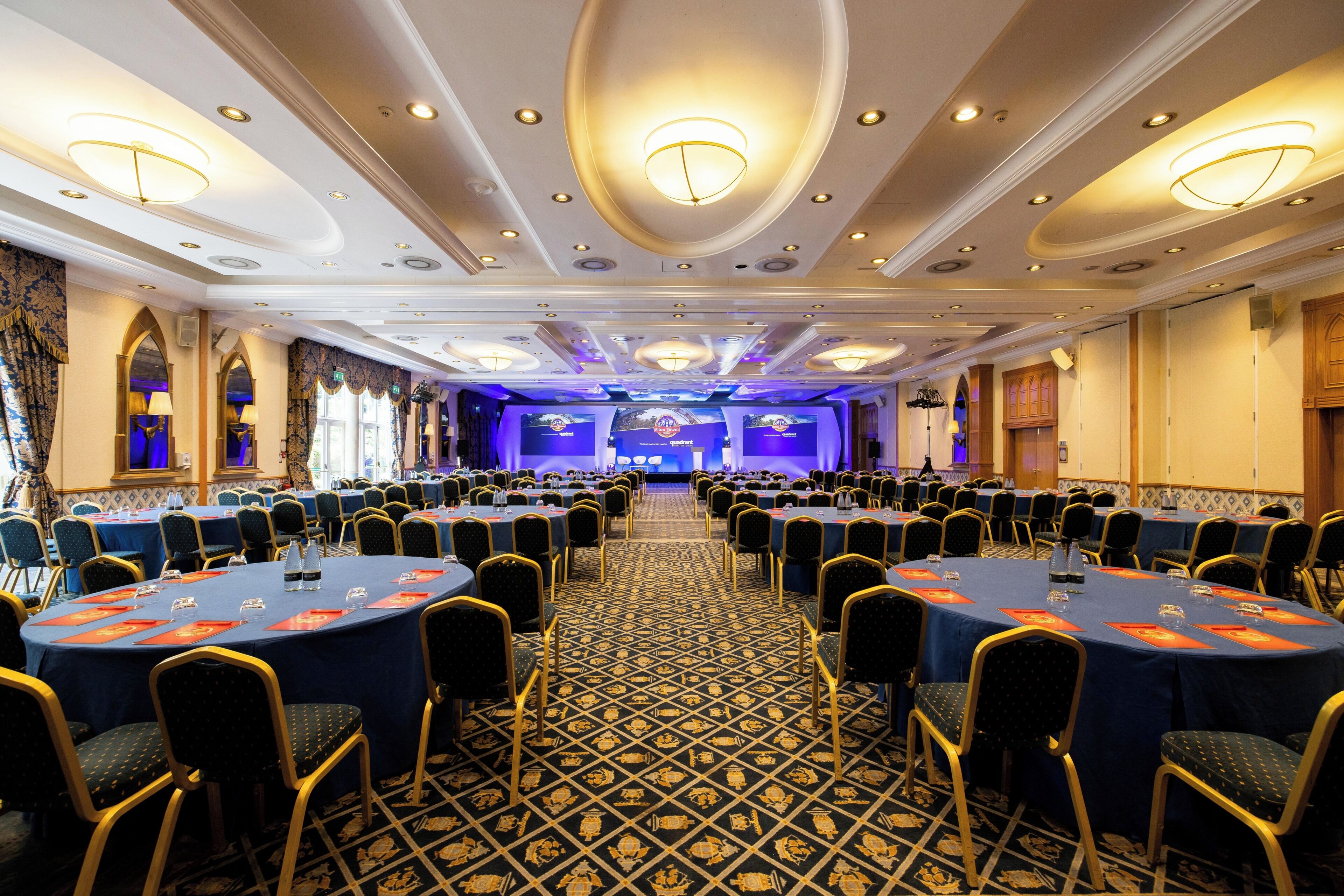 A large conference room with round tables, chairs, and a patterned carpet.