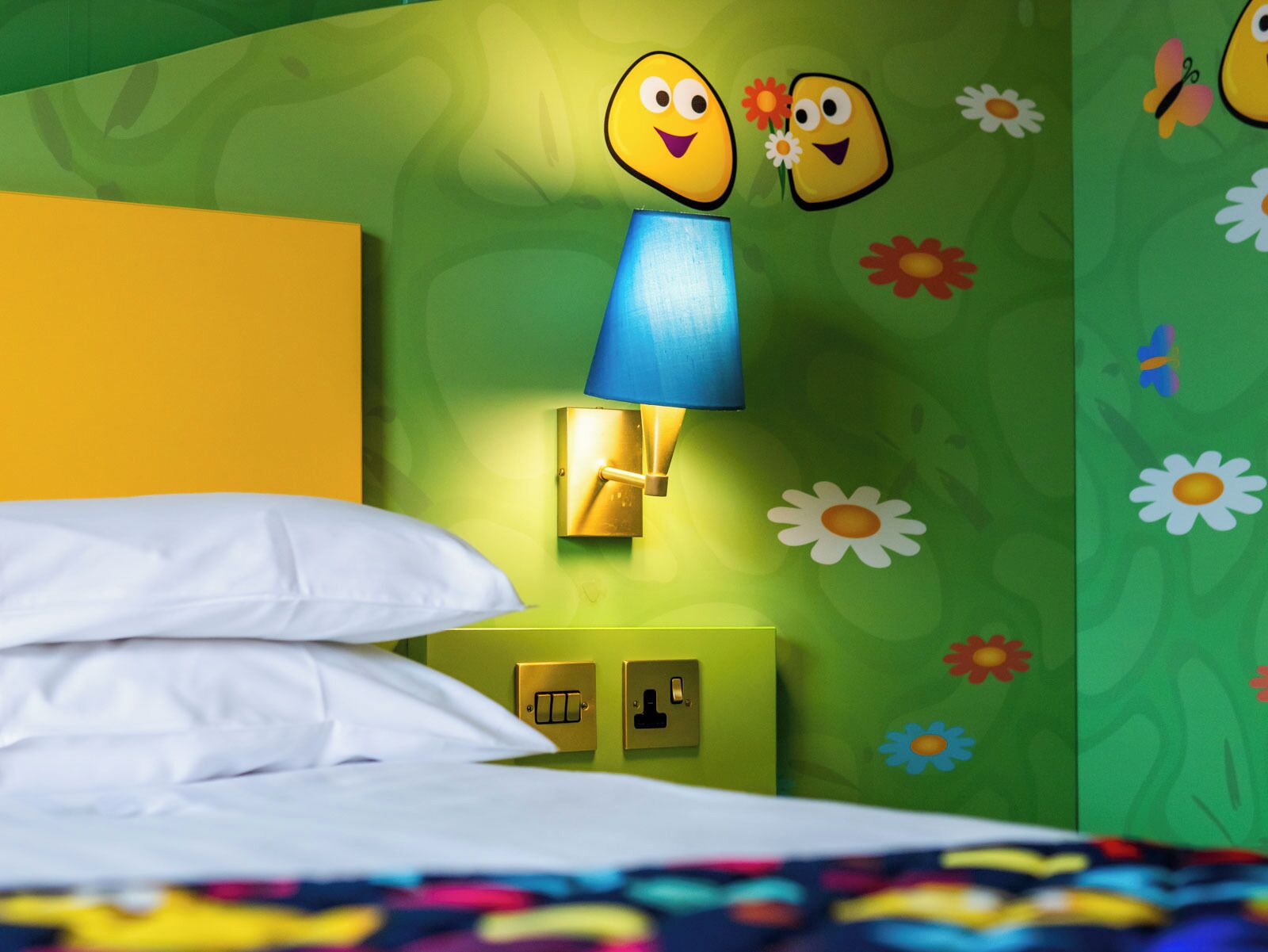 A room with a bed, a wall-mounted lamp, and a nightstand with a switch.