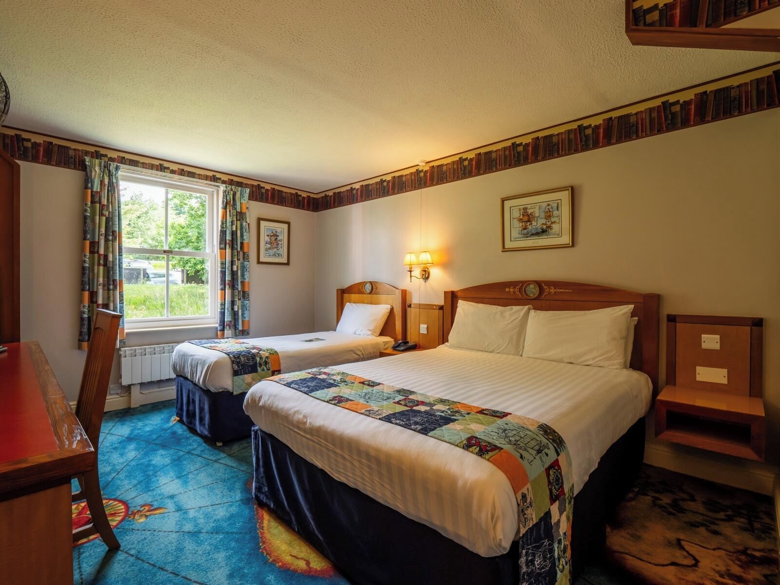 A hotel room with two beds, a desk, and a window with curtains.