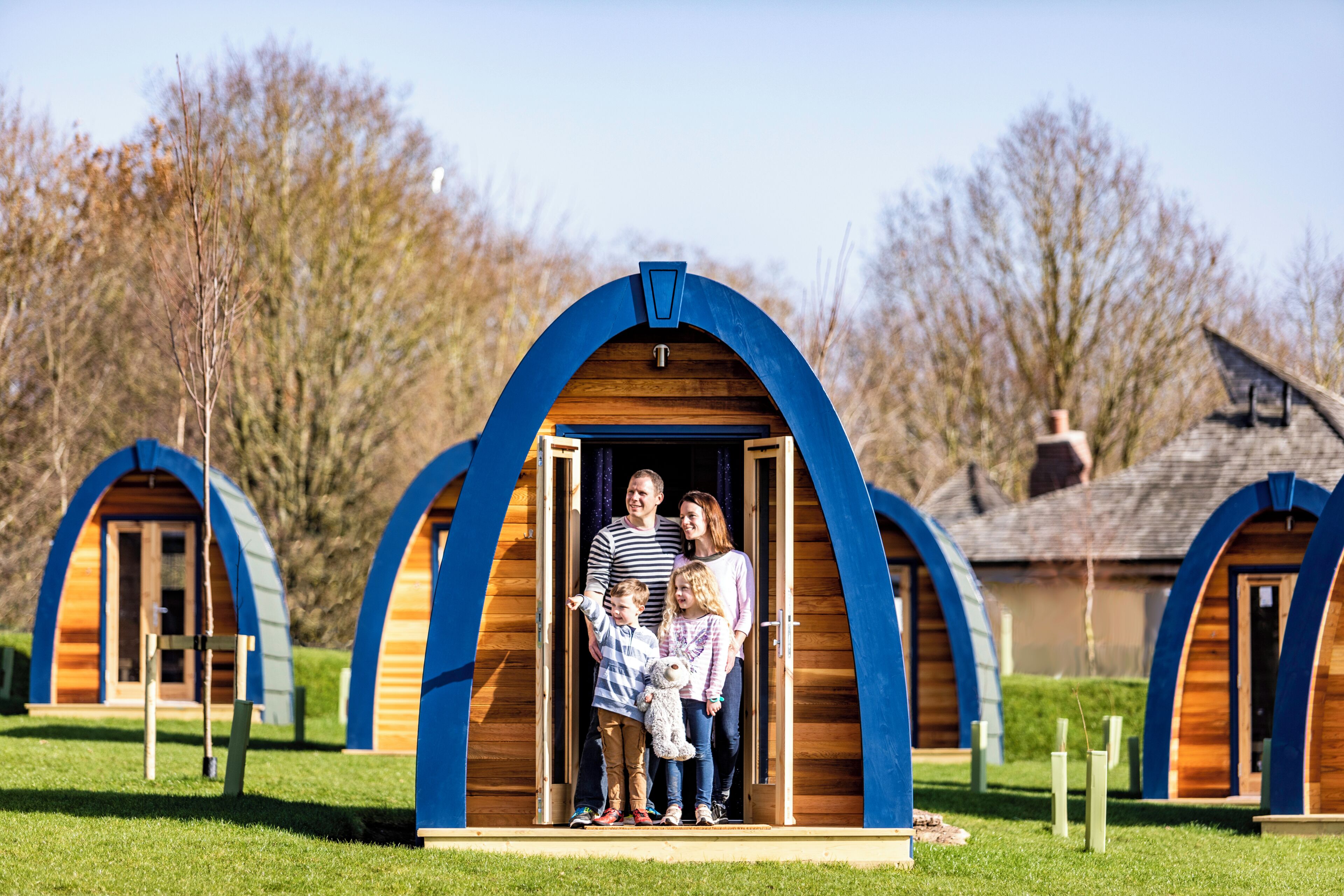 A family standing in an arched wooden structure with a clear sky and trees in the background.