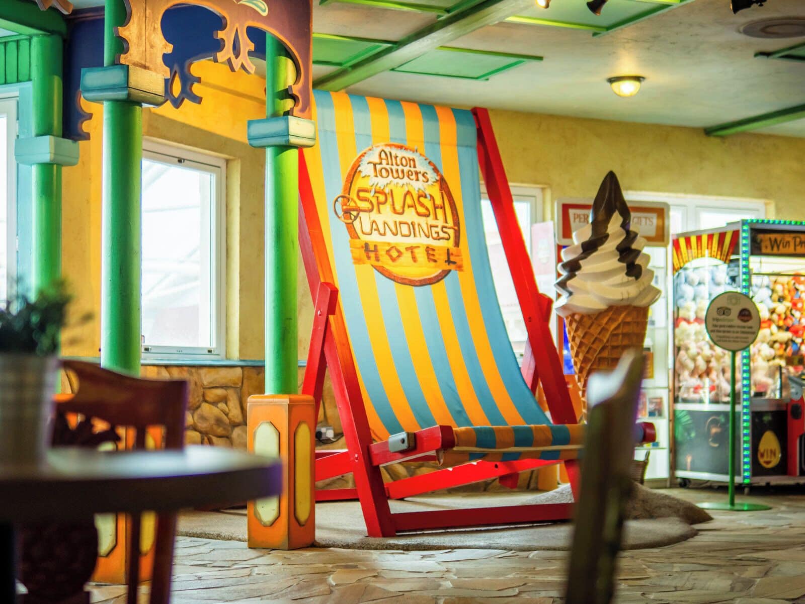 Um sinal colorido com listras para um hotel chamado 'Alton Towers Splash Landings Hotel', com uma grande decoração de sorvete em frente.