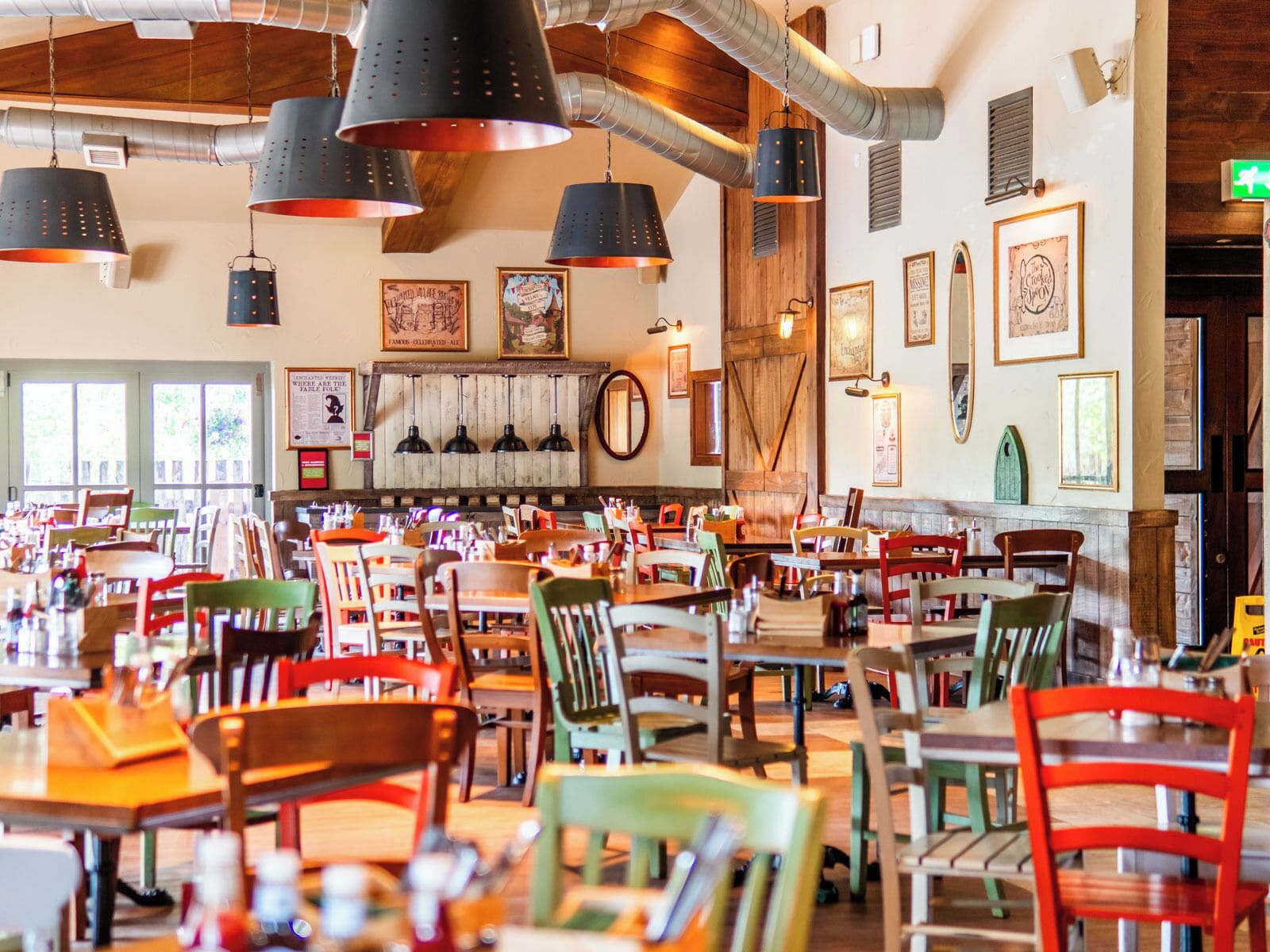 Un interno ristorante con diversi tavoli e sedie, lampade a sospensione e varie cornici alle pareti.