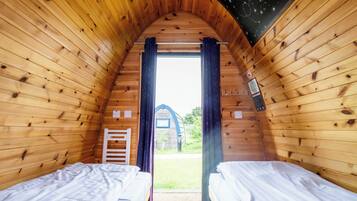 A cozy wooden cabin with two beds, a small window, and a view of the outside.