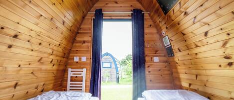 A cozy wooden cabin with two beds, a small window, and a view of the outside.