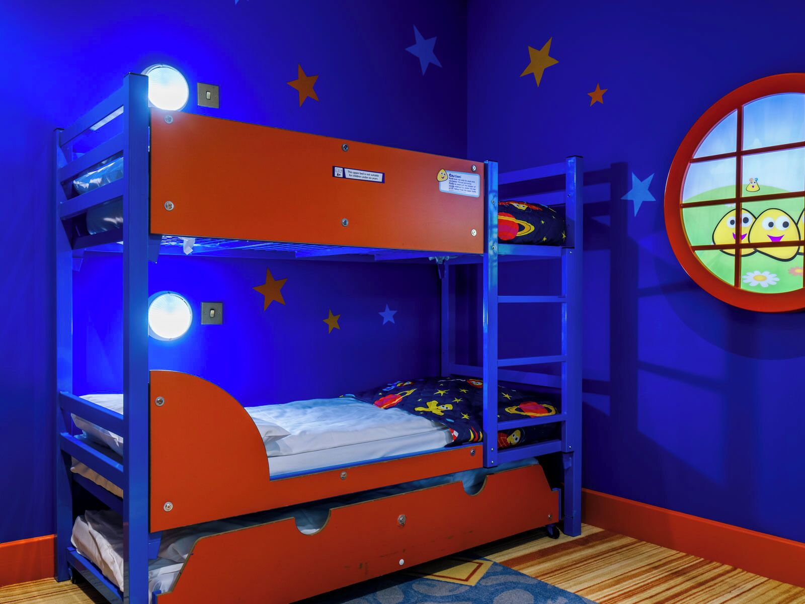 Un lit superposé avec un mur décoré de motifs d’étoiles et une fenêtre ornée d’un personnage de dessin animé.