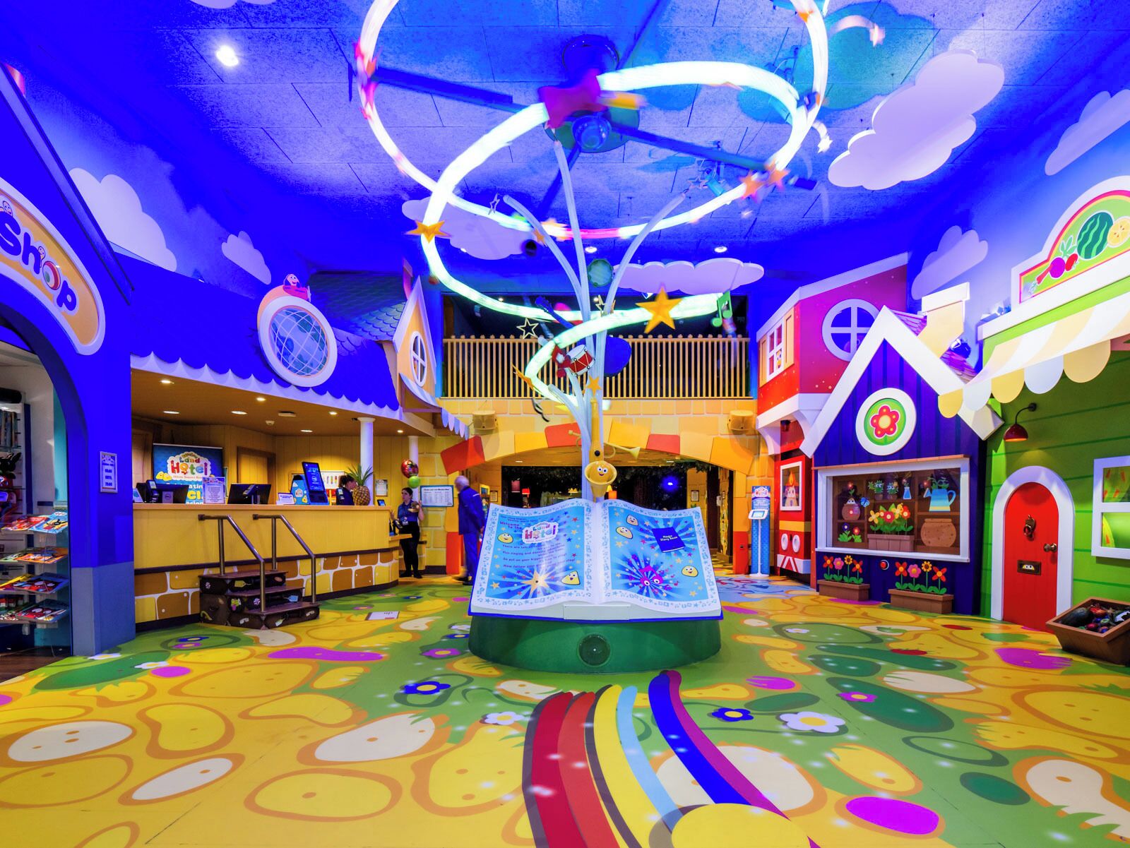 A brightly colored indoor play area with a carousel, a playhouse, and a counter with a menu.